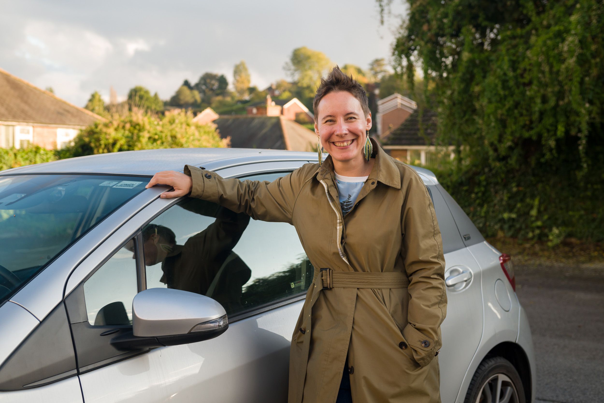 Enthusiastic female Open Homes Nottingham volunteer by her car, contributing to emergency transport services for youth in crisis accommodation.