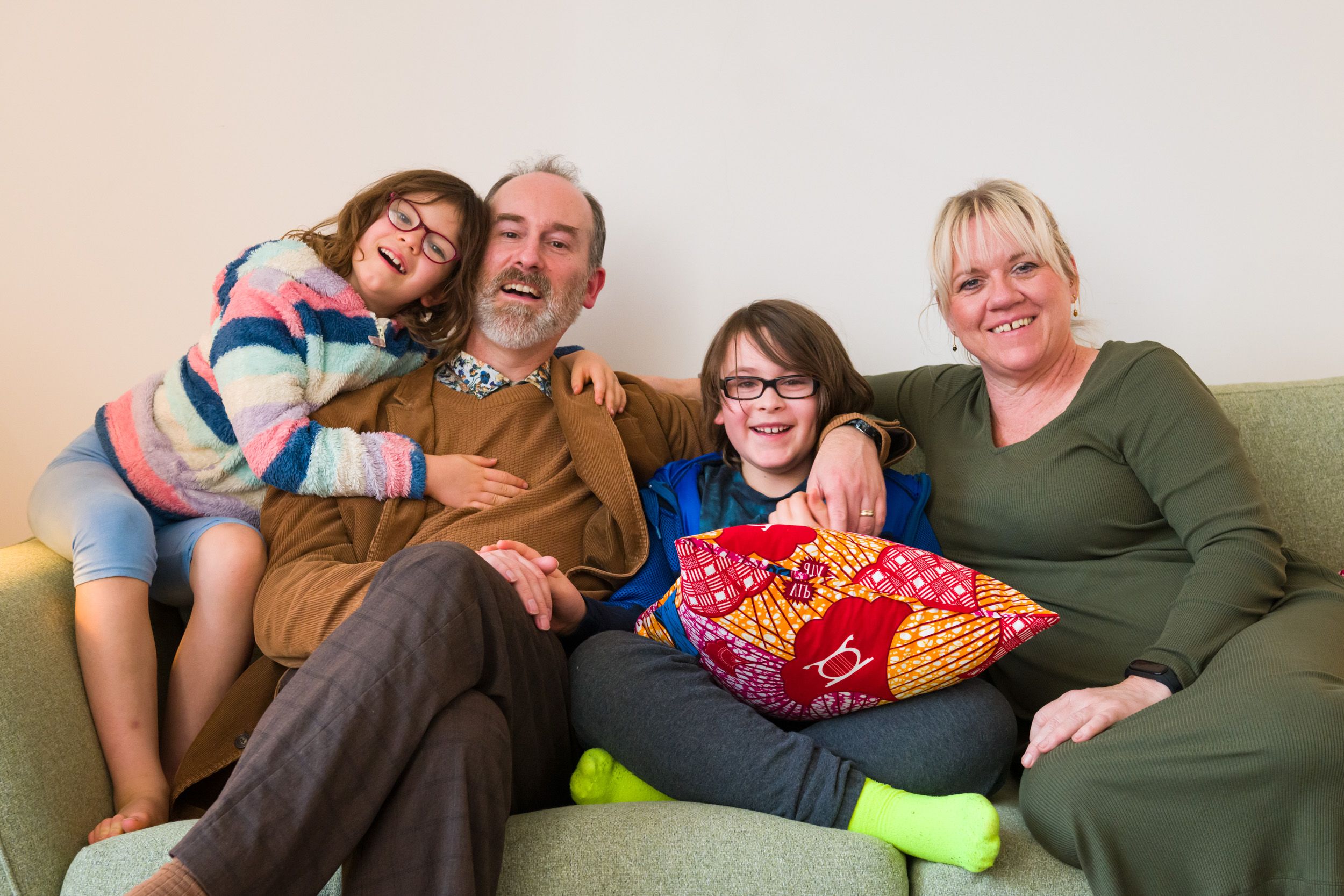 Happy family sitting on a green couch, supported by Open Homes Nottingham charity for young homeless people