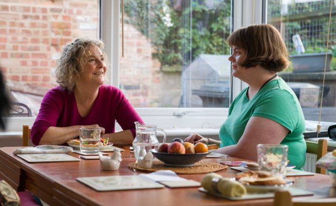 An Open Homes Nottingham volunteer engaging in a heartfelt discussion with a young person over a meal, showcasing the nurturing environment provided for the well-being of homeless youth.