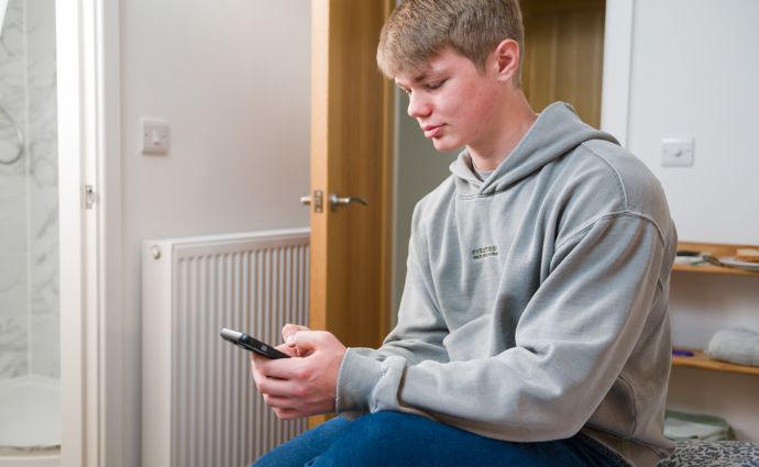 Focused young resident of Open Homes Nottingham using a smartphone to access resources, symbolising the support for connectivity and empowerment.